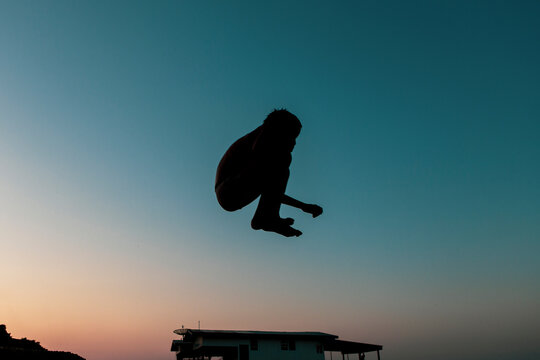 Below above silhouette view of a young boy performing a cannonball in the river Rio Negro at Amazonia, Brazil. Beautiful sunset gradient orange to dark blue color in the background.  Copy space.