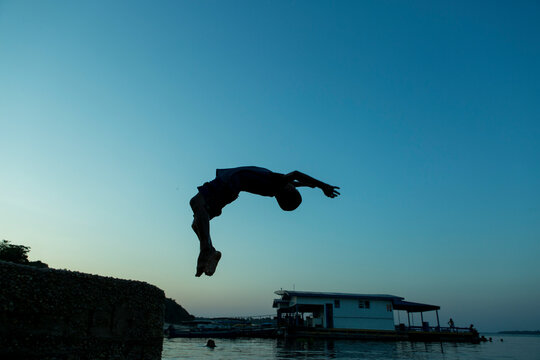 Silhouette view of a young boy performing a backflip jump in the river Rio Negro at Amazonia, Brazil. Beautiful sunset colors in the background. Copy space for text