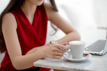 Asian women holding cup coffee with Laptop on table in cafe.Select focus hand holding cup coffee blurred background.