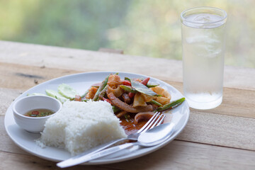 Rice and spicy seafood with water in glass on wooden table.