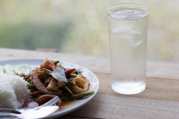 Glass of water with Pad Kra Pao Seafood(Thai food) of rice.