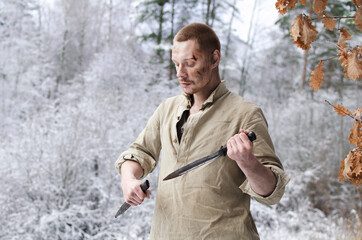 young man in a world war II military uniform with a combat cutlass in his hands in a snowy winter...