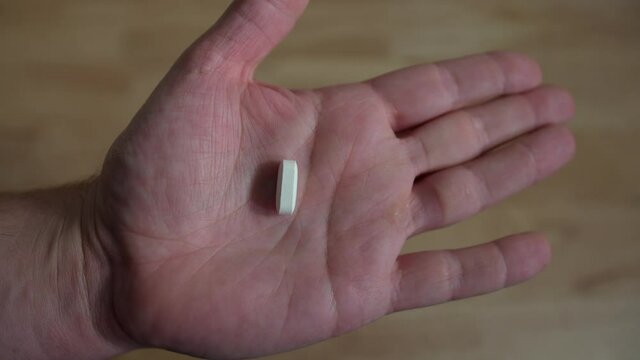 Hand opening up to reveal single white pill in man's hand, closeup 4k medication