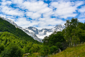 Fototapeta na wymiar A beautiful view of the snow-capped mountain peaks of the Caucasus Mountains. White clouds against the blue blue sky.
