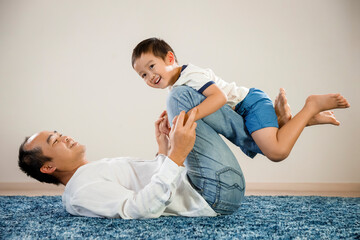 Fototapeta na wymiar Asian father and son portrait, fathers day concept, happy, smiling Vietnamese man sitting on floor with his son in arms, proud parent and child portraiture