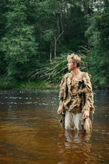 medieval peasant in a ragged raincoat of old sacking wades through the river