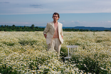 Naklejka na ściany i meble Tall handsome man standing in camomile flowers field