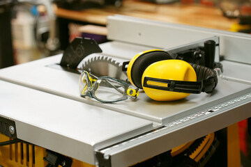 Earmuffs and Safety glasses on Electric saw table in workshop .Work safety concept . selective focus
