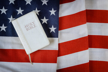 Open is reading Holy Bible book with prayer for america over ruffle American flag in wooden table