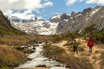 Fototapeta na wymiar dois homens caminhando na trilha com um riacho e uma grande montanha com neve ao fundo