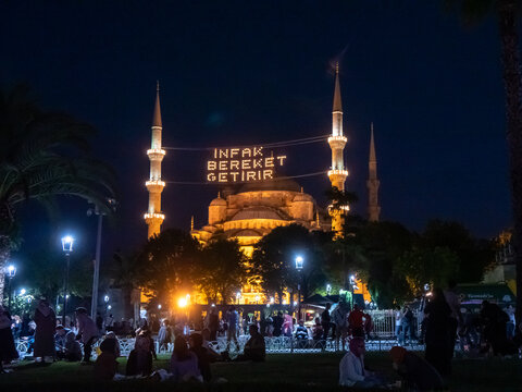 night shot of the blue mosque exterior in istanbul, turkey- mahya says infak bereket getirir in english it means help is bringing blessing .