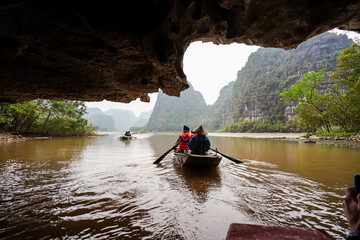 unrecognizable tourists visiting Tam Coc in rowboat passing under natural karst mountain cave