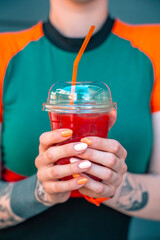 A happy young ginger hipster girl in a dress is holding a cocktail. Close-up pic