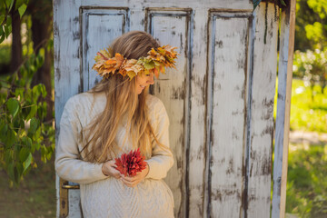 Outdoors lifestyle close up portrait of charming blonde young woman wearing a wreath of autumn leaves. Wearing stylish knitted pullover. Wreath of maple leaves