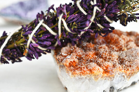 A close up image of a white sage and lilac smudge stick resting on a bright orange cirtine crystal. 