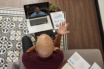 Naklejka premium Young bald entrepreneur actively gesturing when having online meeting with colleague,view from above