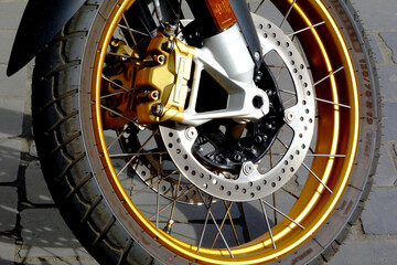 Fototapeta premium Shiny steel brake double discs on modern large motorcycle wheel. mechanical parts. spokes and brake cable. black rubber tire. transportation safety concept. white tube fork. gray cobblestone pavement