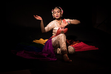Transgender Asian person doing traditional Indian dance in front of a dark black background. Dressed up like an Indian Goddess.