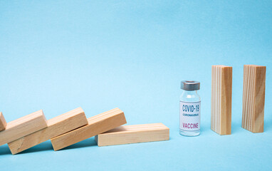 Vaccine concept with wood domino and COVID-19 vaccine ampoule on blue background.
