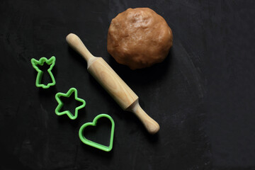 A dough ball, a rolling pin for dough and a cookie shape on a black background. View from above. Cooking ginger biscuits. Christmas atmosphere. Flatlay. Copy space for text. Pastries. Holiday