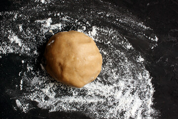 Ginger cookie dough on floured black surface. View from above. The dough has a brown tint. Cooking...