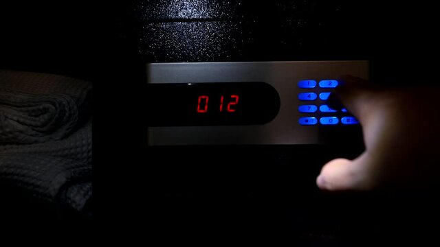 Thief opens the digital safe. Stealing money and valuables at dark night.