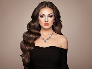 Brunette woman with long and volume shiny wavy hair . Beautiful model with curly hairstyle. Perfect make-up. Beauty style model