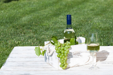 White wine on wooden white vintage table with green lawn on background