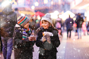 Cute little kids girl and boy having fun on traditional Christmas market during strong snowfall....