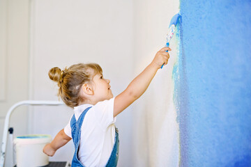 Funny little toddler girl painting the wall with color in new house. Family repair apartment home....