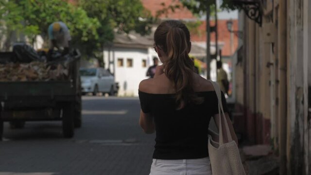 guide goes along street looking for destination against people collecting rubbish in lorry backside view slow motion. Concept travel urban architecture