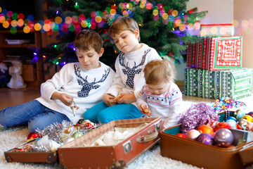 Two little kid boys and adorable baby girl decorating Christmas tree with old vintage toys and balls. Family preaparation celebration of family holiday. Three children, brothers and sister at home.
