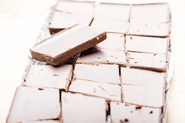 Dark chocolate bar broken into pieces laying in a foil on paper wrap