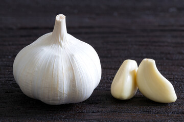 Raw Garlic Bulb and Cloves on dark wooden background..