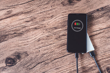 Smartphone charging with power bank on wooden background.