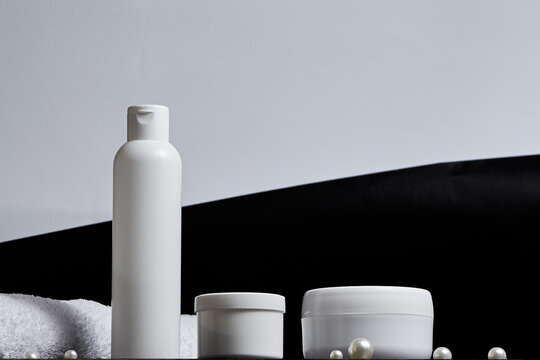 white cosmetic jars for the bath a long tube of pearl towel on a gray and black background. copy space. mockup. bot view