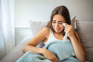 Unhappy millennial girl sit on couch in living room look in distance thinking pondering of...