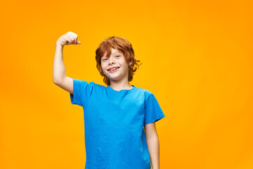 Strong red-haired child shows the muscles of the arms and blue T-shirt 