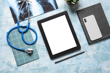 Tablet computer, stethoscope, x-ray image and notebooks on color background