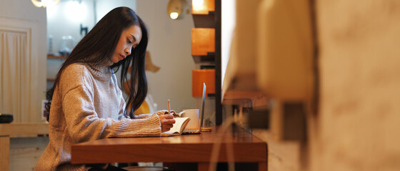 Female university student sitting on counter bar and doing assignment in cafe