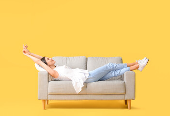 Young woman relaxing on sofa against color background - obrazy, fototapety, plakaty
