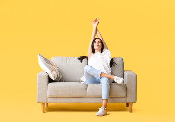 Fototapeta na wymiar Young woman relaxing on sofa against color background