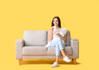 Obraz premium Young woman with tea relaxing on sofa against color background