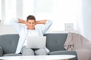 Young man with laptop relaxing on sofa at home