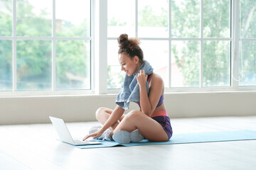 Obraz premium Sporty young woman with laptop resting after training at home