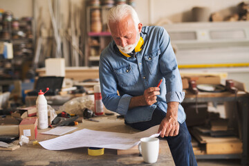 Elderly craftsman holding pencil and reading blueprints