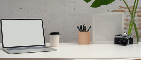 Workspace with mock up laptop, stationery, camera, decorations and copy space on white desk