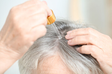 Obraz premium Senior woman using serum for hair loss treatment, closeup