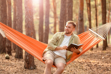 Young man with book relaxing in hammock outdoors
