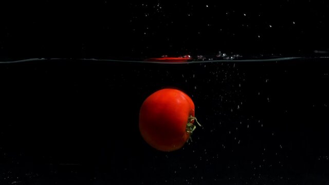 Small tomato falling into the water in front of black screen